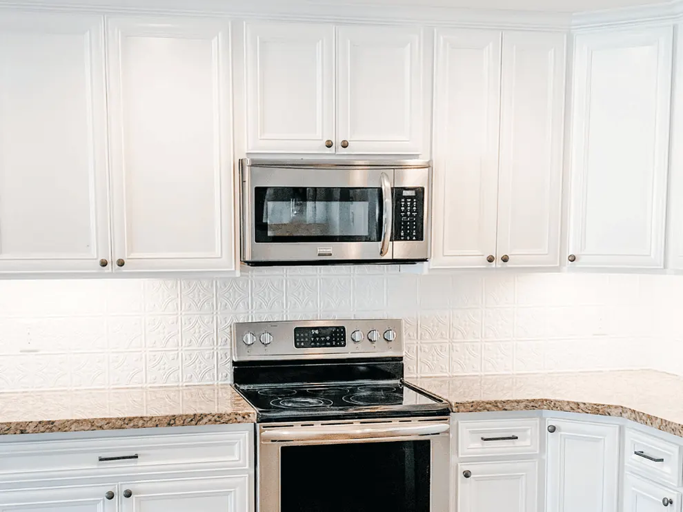 Bright white kitchen cabinets refinished by Jensen Refinishing, with under-cabinet lighting and stainless appliances